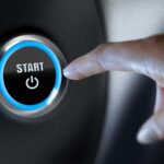a person's hand just about to push the start button of a vehicle, representing their intent to move forward with a purchase